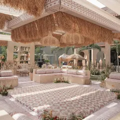 A central seating area for the Haldi ceremony, designed with a custom patterned floor, low cushioned seating, and a thatched roof structure with woven pendant lights.