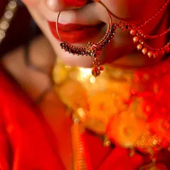 A close-up detail shot of a Bengali bride's nath (nose ring) and bold red lip. This photo emphasizes the traditional jewelry and striking bridal makeup.