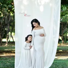 An elegant outdoor maternity shoot with a mother and daughter in matching white gowns. The natural park setting provides a beautiful, serene backdrop for this special moment.