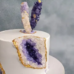 A different angle of the purple geode cake, shot against a lighter background. This view highlights the sparkle of the homemade rock crystals and the clean, sharp edges of the whipped cream frosting.