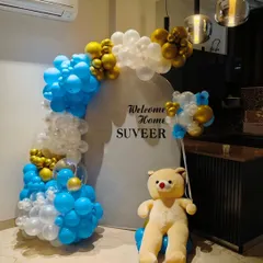 For a modern and clean 'Welcome Home' celebration, I created this setup for baby Suveer. It features a stylish blue, white, and gold balloon arch against a simple white circular backdrop, complemented by a cute teddy bear.