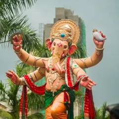 A full view of a magnificent Ganesh idol during the Aagman Sohala, or welcoming procession. The shot is taken from a low angle to emphasize its grand size against the Mumbai skyline.