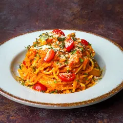 A delicious plate of spaghetti in a bright red tomato sauce, garnished with cherry tomatoes and parmesan, shot with a moody, dark aesthetic.