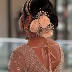 A beautiful bridal updo featuring a combination of fresh white roses and baby's breath. The placement of the flowers creates a delicate crescent shape, perfectly complementing the bride's elegant lehenga.