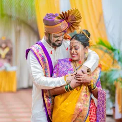 A joyful embrace between the bride and groom, showcasing the vibrant yellow and purple of their traditional Maharashtrian wedding outfits.