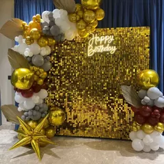 Pure glamour for this birthday bash. A golden shimmer wall provides the perfect sparkling backdrop for an organic balloon garland in gold, white, and grey, complete with a custom neon sign.