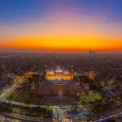An aerial drone view captures the Jama Masjid in Old Delhi during the golden hour of sunset. The entire city seems to glow, with the mosque standing as a beacon of faith and history.