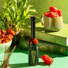 A product shot for Sprig's Bhut Jolokia hot sauce. The vibrant green background and fresh ghost peppers communicate the product's key ingredient and heat.