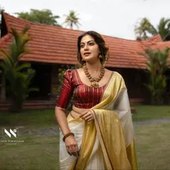 A stunning portrait of Anusree in a traditional Kerala saree with a rich maroon blouse. The setting and the drape come together to create a timeless Onam look.
