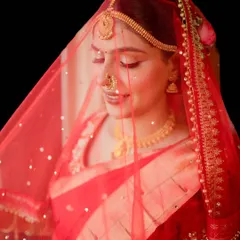 The magic of a classic red bridal look. This shot captures the soft, radiant makeup under a delicate red veil, highlighting a gentle glow and a timeless lip color perfect for the wedding ceremony.