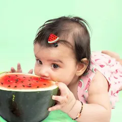 A cute photo of a baby nibbling on a slice of watermelon during her themed photoshoot. This candid moment adds a playful and authentic touch to the collection of milestone pictures.