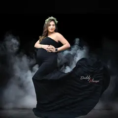 A dramatic studio portrait using a smoke machine for a mystical effect. The mom-to-be stands powerfully in a black gown, creating a striking and memorable image.