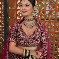 A beautiful bride in a deep wine-colored lehenga, with emerald green jewellery providing a stunning contrast.