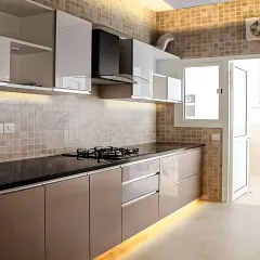 This kitchen showcases a two-tone design with glossy taupe lower cabinets and white upper cabinets. We added under-cabinet lighting to illuminate the countertop and a sleek chimney for ventilation.