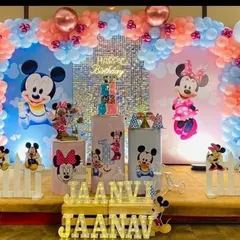 A classic Mickey and Minnie Mouse theme for a first birthday. The setup uses a pink and blue color scheme with a shimmer wall and character cutouts.