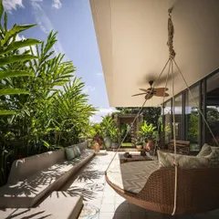 This covered patio at Embassy Boulevard features built-in concrete seating and a hanging swing chair, surrounded by dense greenery to create a comfortable and private outdoor living room.