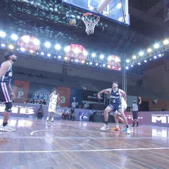 A basketball player executes a perfect jump shot during an Elite Pro Basketball game. The professional court markings and bright overhead lighting ensure optimal playing and viewing conditions.