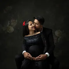 An intimate moment between an expecting couple in our studio. The dark, moody lighting and the woman's elegant black sequined gown create a romantic and glamorous atmosphere for a maternity couple shoot.