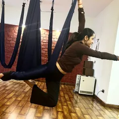A student gracefully holds an aerial warrior pose. This variation challenges balance and strengthens the legs and core.