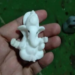 A miniature, unpainted marble-finish Ganesha idol held in hand to show its small scale and fine sculpting details.