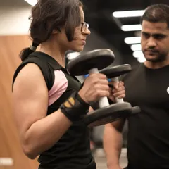 A trainer provides close supervision and guidance to a member performing hammer curls, ensuring her form is perfect for maximum bicep engagement and injury prevention.