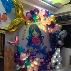 An underwater mermaid theme for a 4th birthday. The circular backdrop features a cute mermaid illustration, framed by a balloon garland with foil mermaid tail accents and a light-up number '4'.