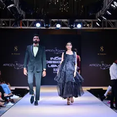 A couple walks the runway for the Indian Designer League (IDL) show. The look features a men's embellished green suit and a women's tiered black gown.