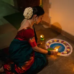 A woman lighting a diya by her rangoli. This photo captures a quiet, traditional moment of Diwali, using the gentle candlelight to create a soft and intimate mood. The gajra in her hair adds a classic touch.