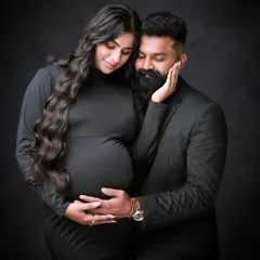 We capture the deep connection between partners with classic, intimate portraits like this one. This couple's portrait, set against a simple dark backdrop, emphasizes emotion and the shared excitement of expecting.
