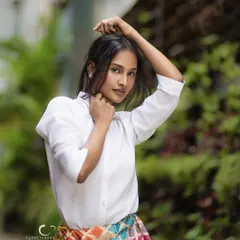 A powerful and engaging portrait set against lush greenery. Her pose is confident, and the natural light beautifully illuminates her features, creating a fresh and striking image.