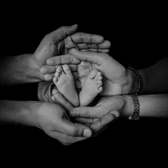 A timeless black and white photograph showing a newborn's tiny feet held securely in the hands of their family. We focus on these small, precious details that tell a big story of love and connection.