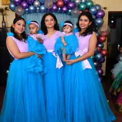 A beautiful family group celebrating together in coordinated outfits. The women wear matching lavender and blue gowns, while the babies have adorable corresponding frocks.