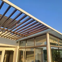 An exterior view of a completed rooftop structure with a wooden slat pergola over a glass roof. This design provides both shade and light, creating a comfortable and stylish outdoor lounge area.
