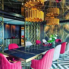 We are drawn to dining rooms that make a bold statement. This space uses dramatic gold chandeliers, a geometric screen, and vibrant pink chairs against a dark, veined marble wall to create an unforgettable, high-energy dining experience.