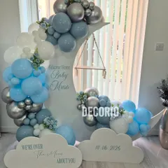 For a dreamy welcome home party, I created this "Over the Moon" setup. It features a custom-built moon prop with a tiny swing, surrounded by a cloud of blue, white, and silver balloons, making it a perfect welcome for a baby boy.
