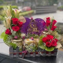 This anniversary hamper is packed in a rustic wooden crate. It's filled with red roses, lilies, jars of nuts, and a large Cadbury Silk heart, making it a truly indulgent gift.
