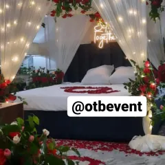 I can turn any bedroom into a romantic escape. This anniversary room decor features a dreamy canopy with sheer drapes and warm fairy lights, surrounded by red roses and a glowing "So Together" neon sign.