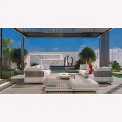 A modern landscape for the Jain residence in Panchsheel Enclave. This view shows the main lounge area on a wooden deck under a pergola, looking out towards a serene water feature and manicured lawn.