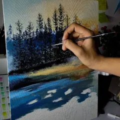 A work in progress shot of an acrylic landscape on canvas. I'm using a fine brush to add details to the trees against the sunset colored sky.