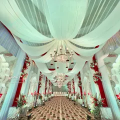A truly grand and regal walkway, with a ceiling of billowing white drapes, crystal chandeliers, and red and white floral accents.
