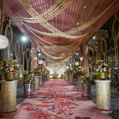 A truly grand entrance for a romantic engagement. A lush pink floral carpet guides guests through a walkway lined with flower-topped pillars, all under a dreamy canopy of draped fabric and hanging crystal chandeliers.