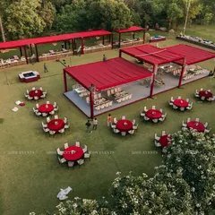 An aerial view of a large-scale outdoor dining setup. The layout includes round guest tables and long buffet stations under elegant red canopies, demonstrating our ability to manage catering and seating for large crowds.