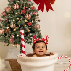 A close-up of the baby's happy face as he sits in the mug, wearing reindeer antlers, perfectly capturing the joy of his first Christmas.