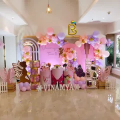 A stunning butterfly and fairy theme for Vinamya's 5th birthday. The decor features elegant arch backdrops, large butterfly wing cutouts, and a beautiful balloon garland in shades of pink, peach, and lavender.