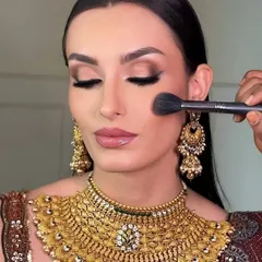 A behind-the-scenes moment from a jewelry campaign. The makeup is designed to complement the intricate gold jewelry without overpowering it.