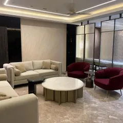 This expansive 9-foot sofa, upholstered in sumptuous suede velvet with bouclé cushions, anchors a luxurious living room. Paired with vibrant red accent chairs and Italian stone coffee tables, it creates a sophisticated space for entertaining.