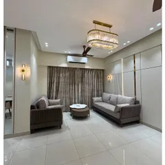 This living room exudes subtle luxury with its neutral-toned sofas, elegant crystal chandelier, and minimalist wall paneling. The design creates a calm and sophisticated atmosphere.