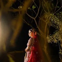 A stunning bridal portrait taken at night in Goa. The bride, in her crimson wedding lehenga, is illuminated against a backdrop of trees, creating a dramatic and enchanting image.