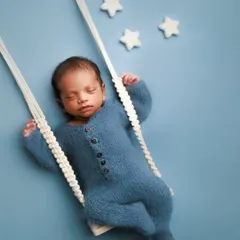 Dreaming in blue. This sweet setup features a baby in a cozy blue romper, seemingly asleep on a miniature swing against a dreamy sky backdrop.