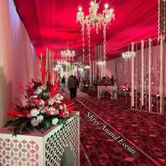 We use bold color and lighting to create immersive entryways. This corridor features rich red draping, patterned flooring, and elegant floral stands under the glow of crystal chandeliers.